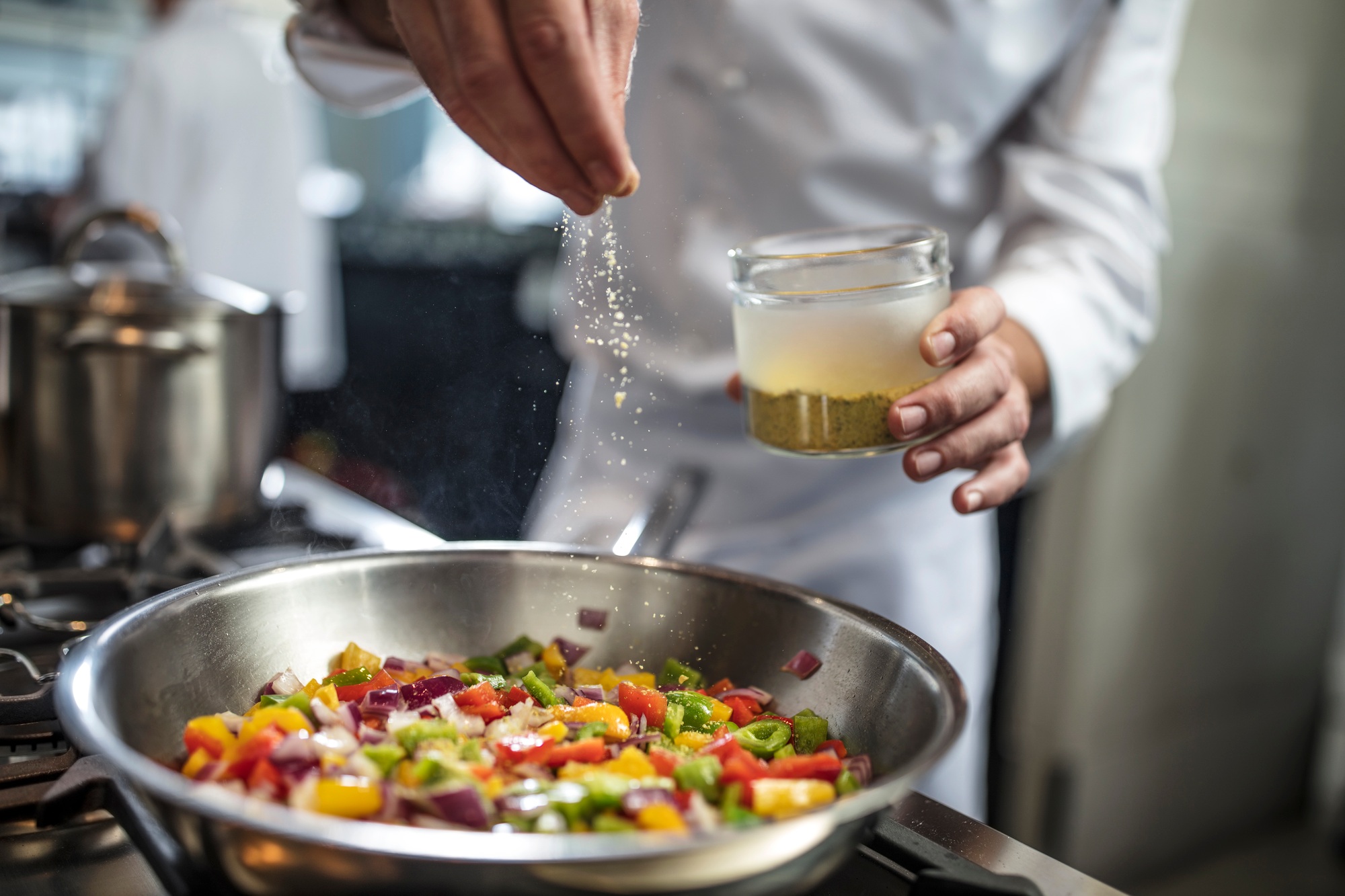 Chef seasoning pan of vegetables on stove, close-up