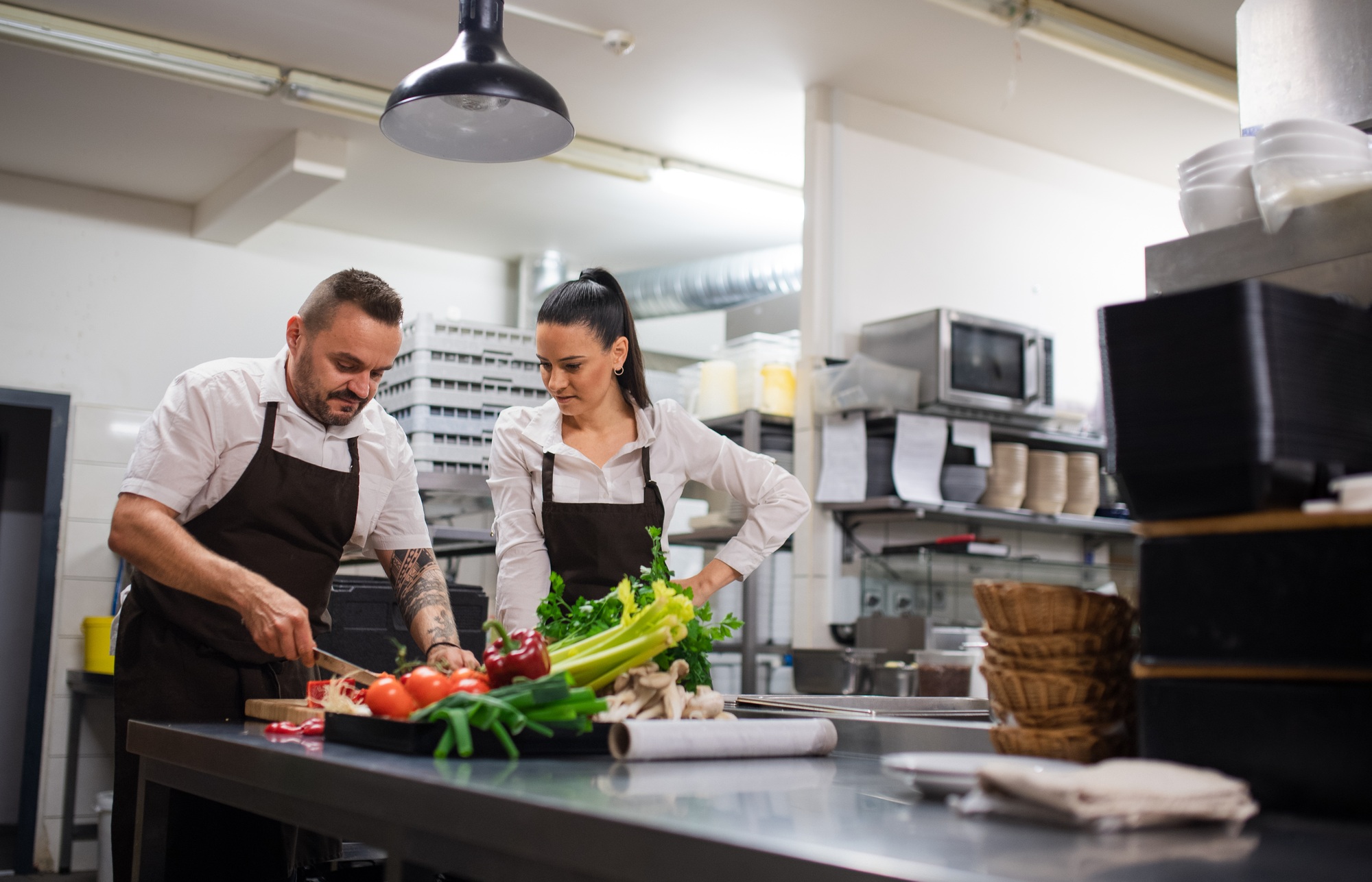 Chef teaching how to cook, cutting vegetables indoors in commercial kitchen